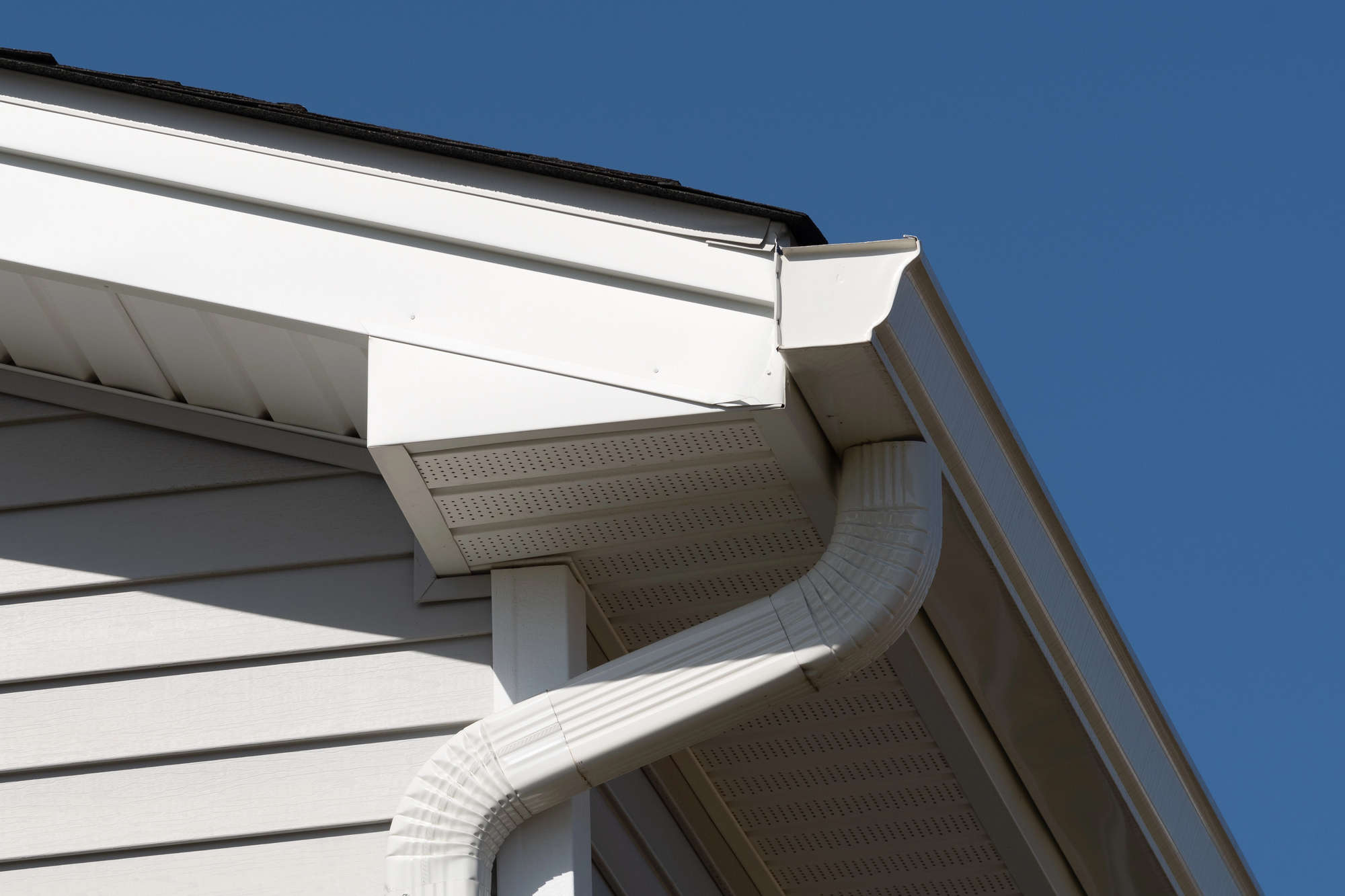 Close-up of a white vinyl-sided home’s roofline showing a white gutter