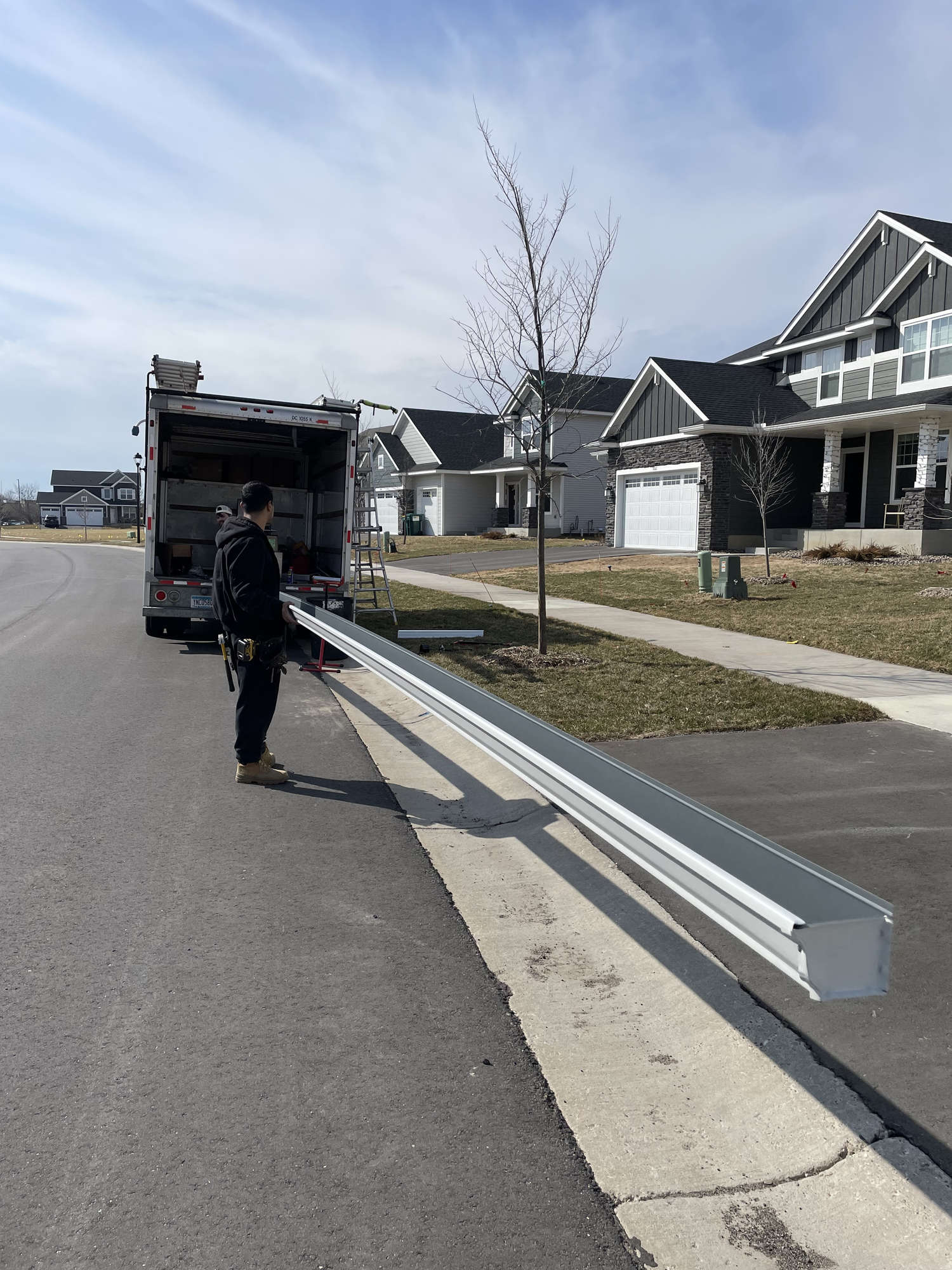 Worker carrying a long gutter section down a driveway