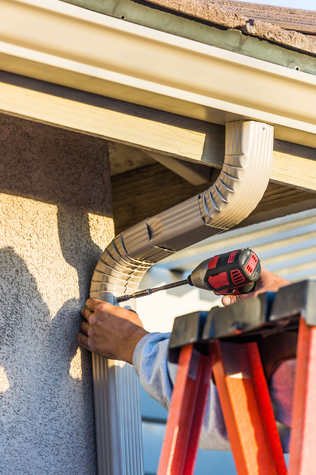 Worker Attaching Aluminum Rain Gutter And Down Spout To Fascia Of House.